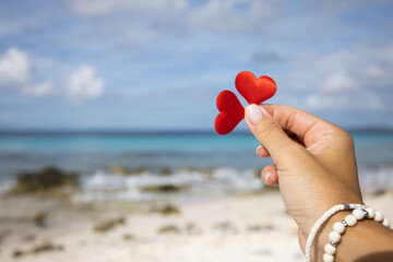 Female hand holding 2 small hearts on the background of the seascape.