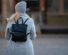 Happy Young Blonde Teenage Girl Going To School Or College Wearing Black Backpack. Blonde Girl In Rgay Hat And Gray Coat. Pictuce From Back