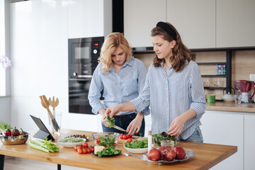 Mom and daughter cooking together in the kitchen. They use vegetables for cooking in a good mood, happy to be together