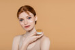© LIGHTFIELD STUDIOS - Pretty young woman with cream on face holding jar isolated on beige