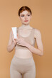 © LIGHTFIELD STUDIOS - Pretty red haired woman holding tube with cosmetic cream isolated on beige