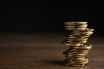 Many coins stacked on wooden table against black background, space for text