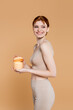 © LIGHTFIELD STUDIOS - Cheerful woman with perfect skin holding container with cosmetic cream isolated on beige