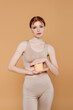 © LIGHTFIELD STUDIOS - Red haired woman holding container with cream isolated on beige