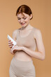 © LIGHTFIELD STUDIOS - Joyful woman in top applying cream on hand isolated on beige