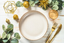 Christmas Table Setting With Luxury Metallic Golden Decorations And Eucalyptus Leaves. Top View At White Table.