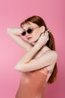 © LIGHTFIELD STUDIOS - Stylish woman in sunglasses adjusting hair isolated on pink