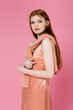 © LIGHTFIELD STUDIOS - Pretty red haired woman in peach dress and sweater looking at camera isolated on pink