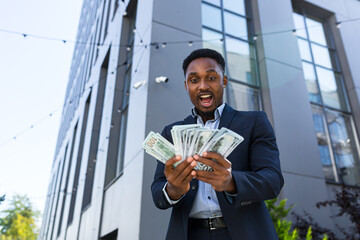 Happy successful African American businessman counts, waves, throws, show off, flaunt, cash money background a modern office building looking at camera Celebrate Winner success in betting stock market