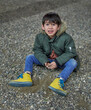 latino child staring at the camera with tears, very sad and anguished, sitting on the floor in a park. Vertical
