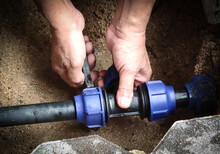 Close-up Of Hands Fixing Water Pipe. Plumber Fixing Underground Pipe With Tools.