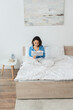© LIGHTFIELD STUDIOS - cheerful young woman in pajamas reading travel life newspaper and holding cup in bed.