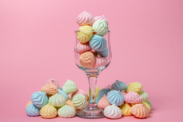 Wall Mural - Multicolored meringues on a pink background. Glass goblet overflowing with colored meringues.