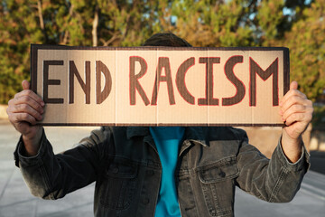Young man holding sign with phrase End Racism outdoors