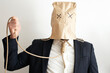 business man in dark suite and a paper bag over it's head, trying to hang himself with a jute rope