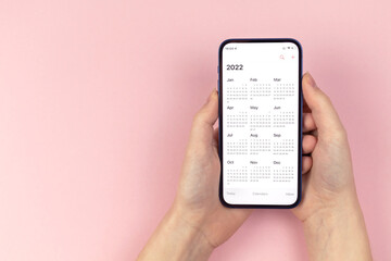 Calendar 2022. Smartphone in woman hands. Pink background, workspace, to do, new year planning concept photo