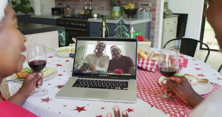 Wall Mural - African american couple with wine using laptop for christmas video call with happy family on screen