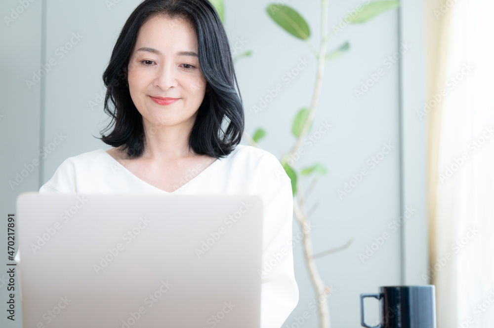 俯きパソコンで仕事をする美しいアラフォーのアジア人(日本人女性)   コピースペースあり