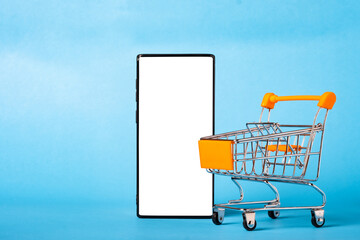 empty orange Shopping cart with white screen mobile smart phone on light blue background with copy space for text. banner shopping for store or supermarket.