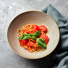 Wall Mural - Vegetarian appetizing pasta served with tomato sauce, basil and fresh cherry tomatoes on ceramic plate. Light grey concrete background. Top view.