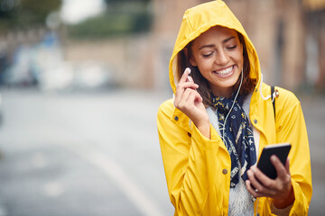 Wall Mural - A young girl with yellow raincoat is walking the city while listening to the music on the rain. Walk, rain, city