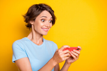 Poster - Profile side photo of young girl happy positive smile excited crazy play game cellphone isolated over yellow color background