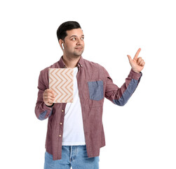 Wall Mural - Young man with book and earphones pointing at something on white background