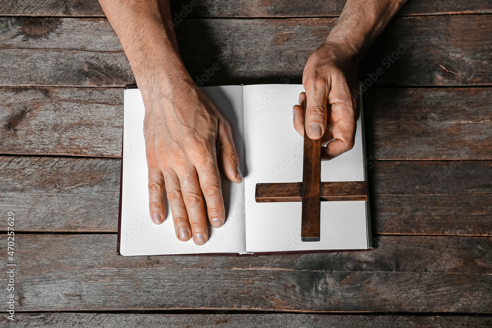 Man with cross and open Holy Bible on dark wooden background