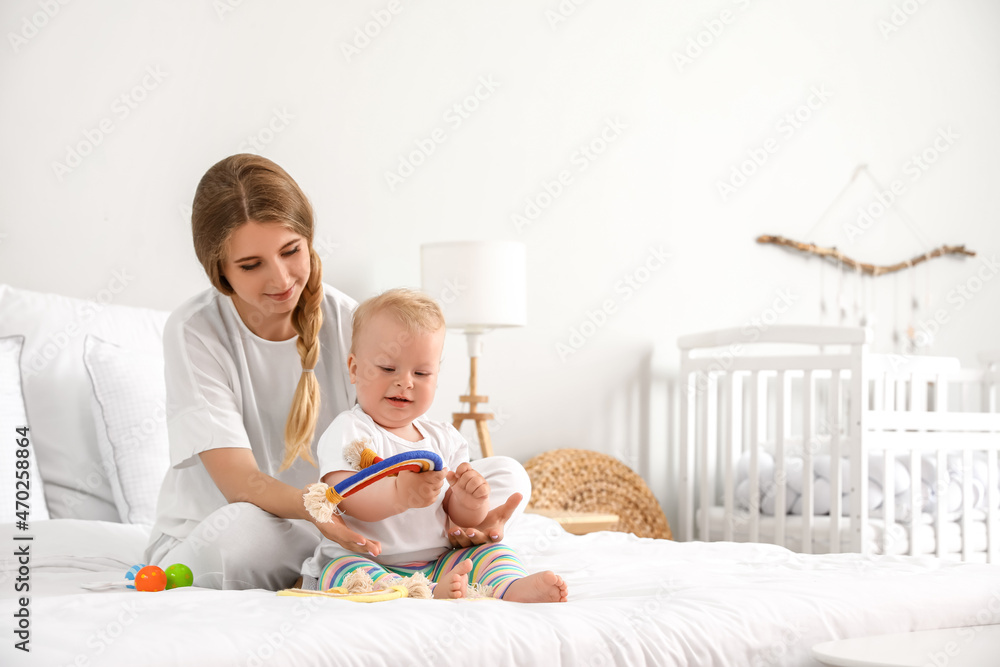 Young mother playing with her cute little baby on bed