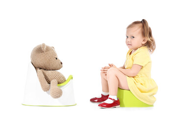 Wall Mural - Cute baby girl and toy bear sitting on potties against white background