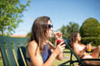 © KAMPUS - Peaceful woman drinking bright cocktail. Woman in blue swimsuit sitting on deck chair. Female friend lying in background. Leisure, friendship, party concept
