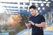 © Liubomir - A healthy man watches a video on a mobile phone after a workout while sitting outdoors using an app on a 4g wireless device. Asian athlete is happy and smiling after running rest