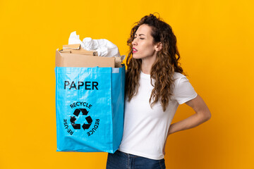 Wall Mural - Young woman holding a recycling bag full of paper to recycle isolated on yellow background suffering from backache for having made an effort