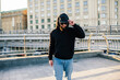 © San4ezz007 - City portrait of handsome hipster guy wearing black blank hoodie with space for your logo or design. Mockup for print