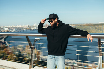 Wall Mural - City portrait of handsome hipster guy wearing black blank hoodie with space for your logo or design. Mockup for print