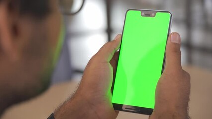 Business man holding phone in hand with green mockup empty blank cellphone screen template using mobile app, smartphone application advertisement, over shoulder closeup view.