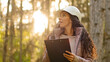 © Yuliia - Female technician with clipboard taking measures for reforestation of woodlands. Forest evaluation and management. Millennial indian Forestry engineer in hardhat in park during logging deforestation