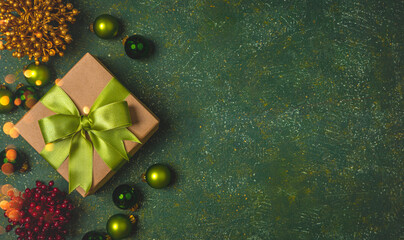 Christmas gift box with green ribbon and green christmas balls on the green stone background