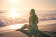 Young woman sitting on the beach looking at the ocean, Malibu, Los Angeles, California