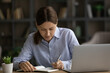 © fizkes - Concentrated serious young woman sit at desk near laptop jotting information in notebook. Making important notes, write personal records to daybook, keep a diary, create business to-do list concept