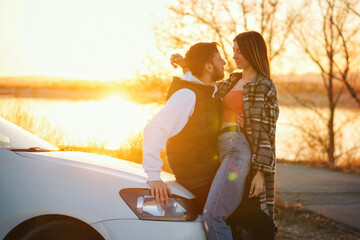 Wall Mural - Man and woman in holiday honeymoon trip. Couple is hugging in sunset near car outdoors. Lovers traveling together. Lifestyle Candid portrait. Romantic sunset journey