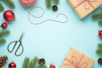 Wall Mural - Top view photo of pine twigs cones red christmas tree balls scissors spool of decorative rope and two craft paper gift boxes on isolated pastel blue background with copyspace in the middle