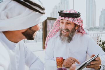 Senior and young arabian men wearing kandura traditional dress from uae in Dubai. Speaking about business plans