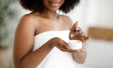 Cropped View Of Young African American Woman Using Hydrating Cream, Wearing Bath Towel Indoors, Closeup