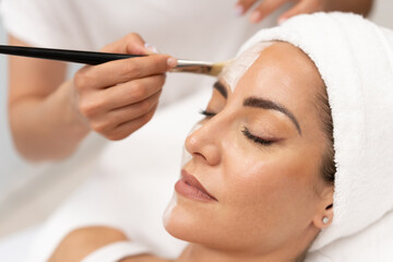 Wall Mural - Aesthetics applying a mask to the face of a Middle-aged woman in modern wellness center.