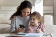 © fizkes - Happy mother with daughter distracted from drawing with colorful pencils using smartphone, enjoying leisure time with gadget, smiling mom and adorable girl kid having fun online or watching tutorial