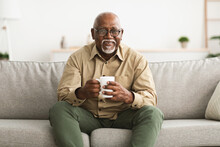 Mature Black Man Drinking Coffee Sitting On Sofa At Home