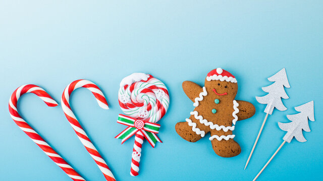 composition of christmas lollipops, gingerbread man and christmas trees on blue banner