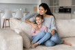© fizkes - Smiling dreamy woman with cute little daughter kid visualizing good future, sitting relaxing on cozy couch at home, looking to aside, happy young mom with adorable girl child dreaming together