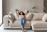 Fototapeta  - Smiling barefoot woman resting on comfortable couch at home alone, happy beautiful young female with closed eyes stretching, daydreaming or taking day nap, enjoying leisure time, no stress concept